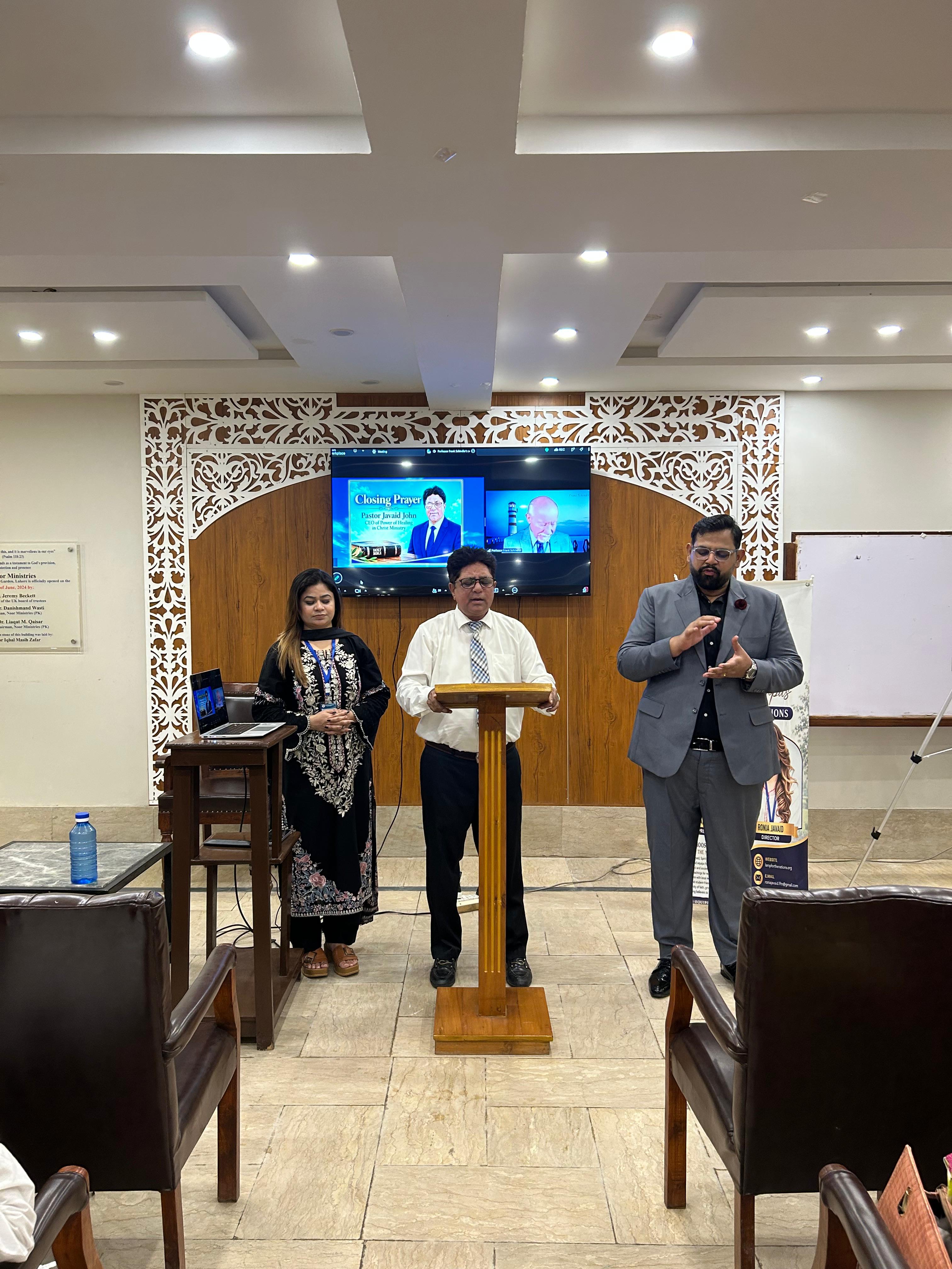 Leaders at the podium during orientation, with a closing prayer on the screen behind them